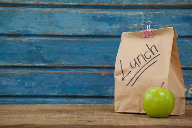 Papierowa torba na lunch, obok zielone jabłko na niebieskim tle, Adobe Stock